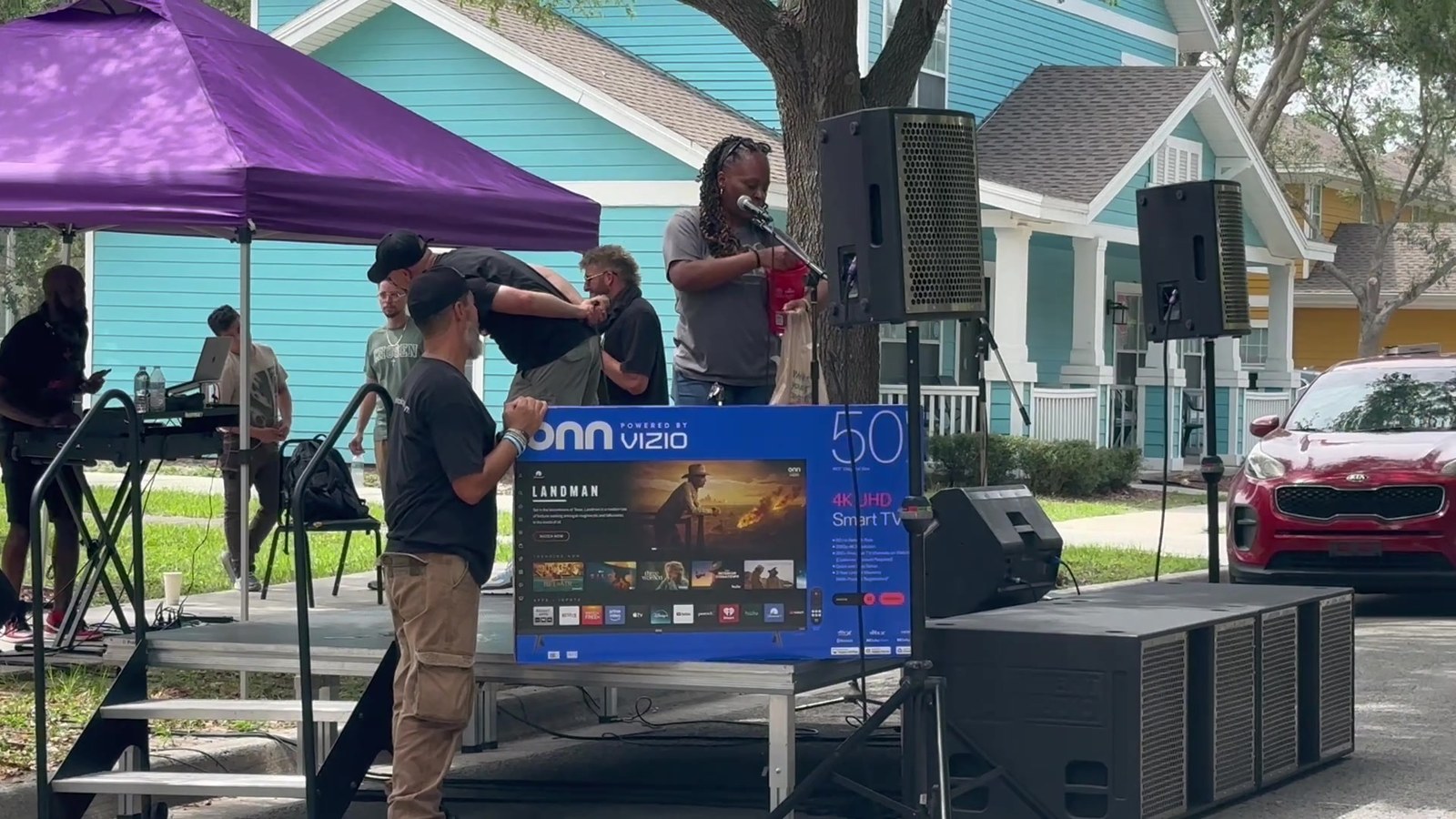 A live performer sings at a community day event, with a 50-inch TV set up for a giveaway to residents