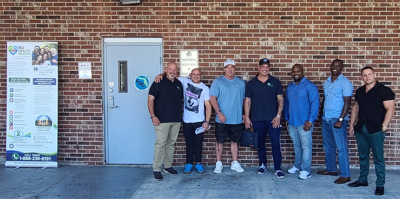 A group of outreach partners standing together outside a Florida Department of Corrections re-entry facility next to a NuHealth Reach informational banner