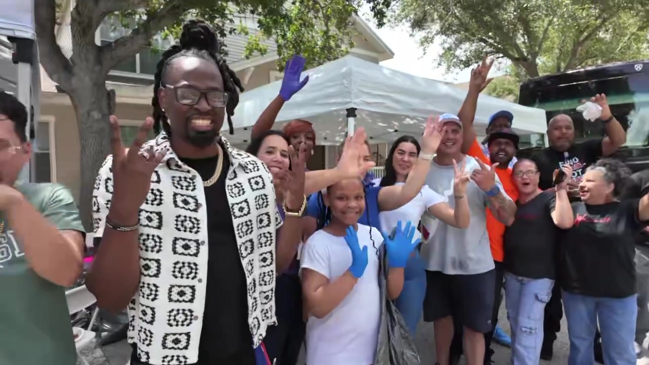 A diverse group of volunteers and neighbors waving and cheering together at an outreach event